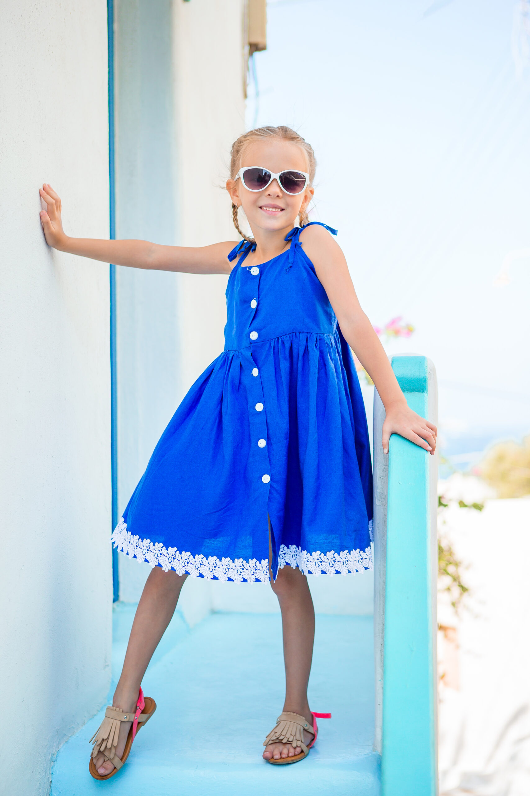 Little adorable girl in dress outdoors in old streets an Mykonos. Kid at street of typical greek traditional village with white walls and colorful doors on Mykonos Island, in Greece